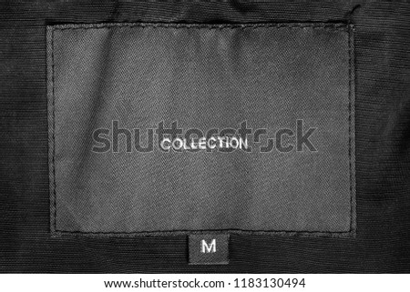 M size clothes label says collection on black textile background closeup