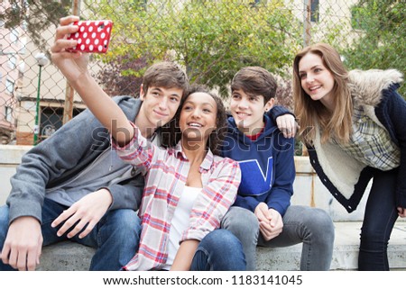 Group of diverse teenagers together in urban city using smartphone taking selfies photos with fun expressions, fashionable friends outdoors. Adolescents networking technology, recreation lifestyle. 