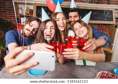 Happy friends with party accessories holding red glasses, making selfie and having fun