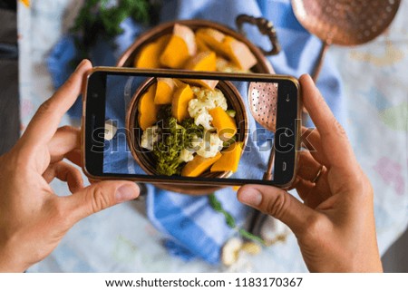 Woman hands takes photography of food on table with phone. Dinner, lunch. Cooked steam vegetables. Smartphone photo for social networks or blogging post. Vegetarian, healthy, organic