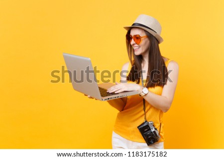 Traveler tourist woman in summer casual clothes, hat holding laptop pc computer isolated on yellow orange background. Girl traveling abroad to travel on weekends getaway. Air flight journey concept