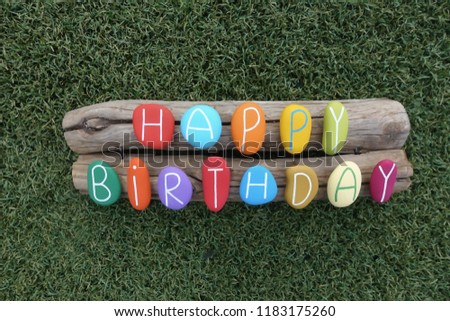 Happy Birthday stones over two pieces of wood with grass background
