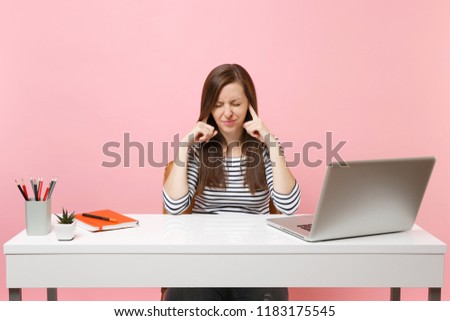Dissatisfied woman with closed eyes does not want listen covering ears with finger sit work at white desk with contemporary laptop isolated on pink background. Achievement business career. Copy space