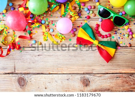 Border of colorful party accessories, balloons, candy and confetti for a Mardi gras or carnival on rustic wood with copy space