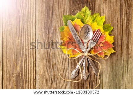 Autumn dinner place setting for Thanksgiving holiday with colorful maple leaves on rustic wooden boards, toned