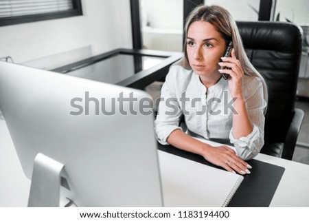 Woman talking on the phone sitting at the computer at the workplace in the office