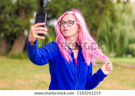 selfie concept of ukrainian beautiful girl portrait  with simple make up pink hair and glasses taking photo by herself on black mobile phone device