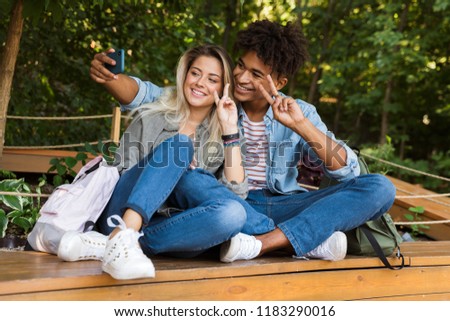 Excited young multiethnic couple talking while spending time together at the park, taking a selfie