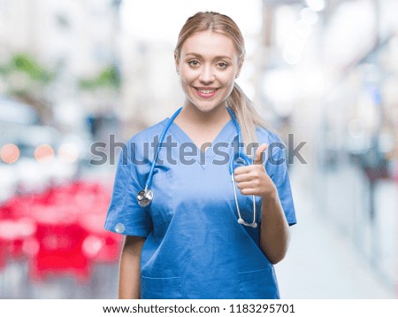 Young blonde surgeon doctor woman over isolated background doing happy thumbs up gesture with hand. Approving expression looking at the camera with showing success.