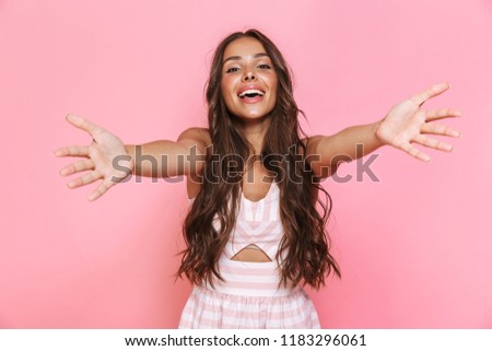 Image of happy young woman 20s with long hair wearing dress laughing and reaching arms towards you isolated over pink background