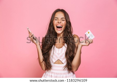 Photo of cheerful woman 20s wearing dress holding mobile phone and credit card isolated over pink background
