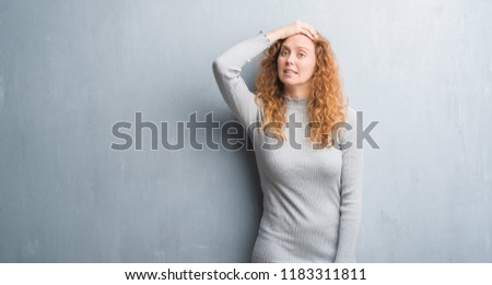 Young redhead woman over grey grunge wall stressed with hand on head, shocked with shame and surprise face, angry and frustrated. Fear and upset for mistake.