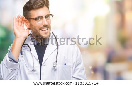 Young handsome doctor man over isolated background smiling with hand over ear listening an hearing to rumor or gossip. Deafness concept.