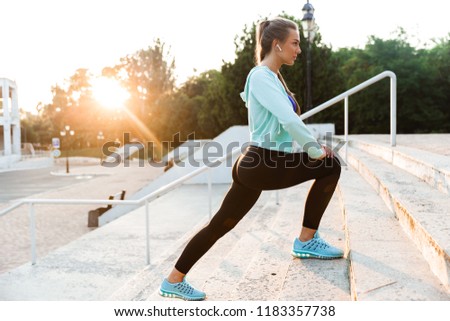 Photo of concentrated young sports woman in park outdoors make sport stretching exercises.