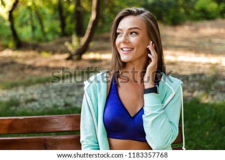 Photo of beautiful young sports woman in park outdoors listening music with earphones.