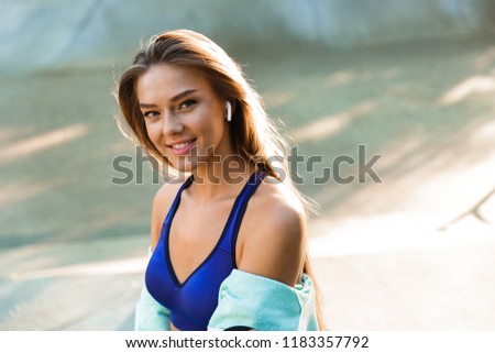 Photo of beautiful young sports lady in park outdoors listening music with earphones.