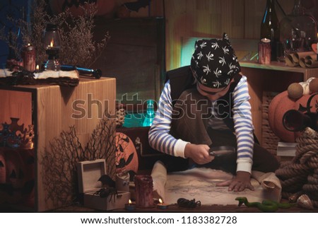 Boy in pirate costume for Halloween exploring map with magnifying glass