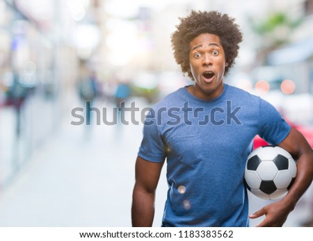 Afro american man holding football ball over isolated background scared in shock with a surprise face, afraid and excited with fear expression