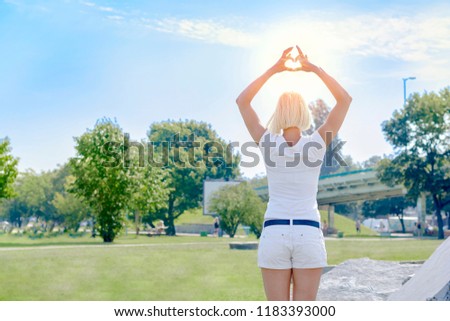 Young woman standing and holding hands in heart shape framing on sky background