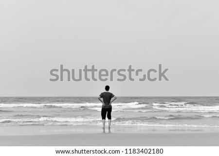 young boy alone  stand near the beach and sea waves, black and white photography.