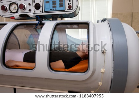 beautiful girl in a black T-shirt and white pants lies in a hyperbaric chamber Royalty-Free Stock Photo #1183407955