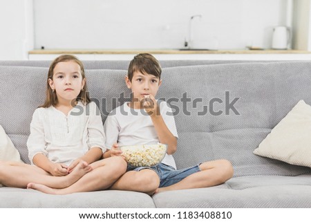 Little girl and little boy enjoy eating popcorn and watching tv at home.Leisure time for children
