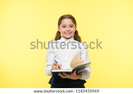 Write note to remember. Child school uniform smart kid happy make note. Girl happy face make note about idea yellow background. Child girl happy school uniform clothes holds book ready write note.