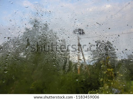 Stork nest and green trees behind the wet glass in autumn rain drops. Rainy day in countryside.