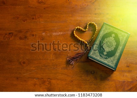 Koran and rosary isolated on wooden background. Arabic word translation : The Holy Al Quran (holy book of Muslims) - it's public item of all muslims. Islamic concept