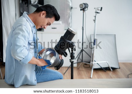 Young Vietnamese photographer cleaning lightning equipment in studio