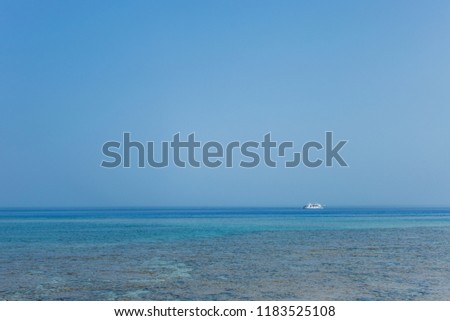 White ship in distance. Blue marine water and clear sky background. Horizontal color photography.