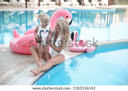 Beauty fashion mother with daughter family look. Beautiful blonde pretty woman having fun with adorable little girl  wears in white swimwear having fun by swimming pool on luxury resort. 