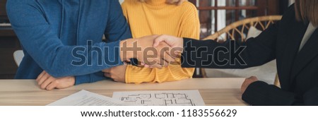 Happy young Asian couple and realtor agent. Cheerful young man signing some documents and handshaking with broker while sitting at desk. Signing good condition contract.  Panoramic banner background.