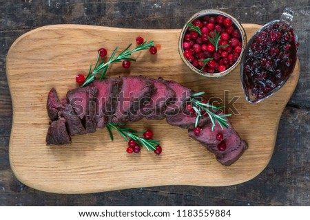Sliced venison steak on wooden board with lingonberries - top view