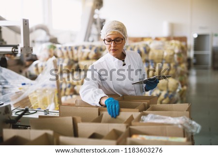 Young female employee in sterile clothes is checking packages ready to be delivered.