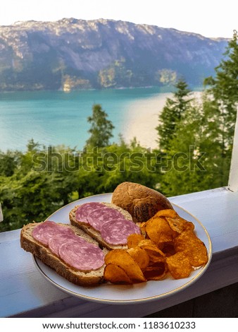 A snack meal of bread, salami, and crisps, with a beautiful Norwegian fjord in the background