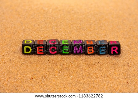 The word december is composed in colored letters on black cubes and lie on the sand.