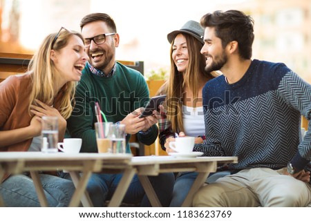 Group of four friends having a coffee together. Two women and two men at cafe talking laughing and enjoying their time using digital tablet. Royalty-Free Stock Photo #1183623769