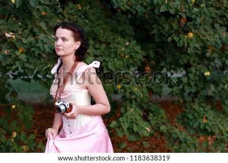 Fine emotional brunette with vintage photo camera. Yonge girl in vintage pink pastel with live expressions on beautiful country and old background.