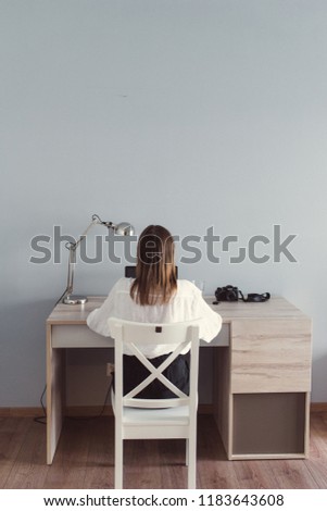 Young woman in white blouse working at the table, photo camera next to laptop. Business woman working on laptop in lite interior. Photographer editing pictures on laptop. Woman studying at the table