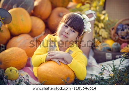 
A little girl with pumpkins and other vegetables and fructomes in honor of Thanksgiving. Girl playing outdoors. A child with a pumpkin in her hands
