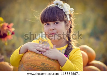 
A little girl with pumpkins and other vegetables and fructomes in honor of Thanksgiving. Girl playing outdoors. A child with a pumpkin in her hands