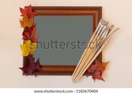 Picture frame, paint brushes and colorful autumn leaves on pastel background