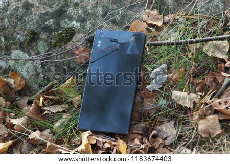 A lost mobile phone liying on ground near a stone in forest.
