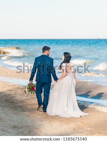 Cheerful married couple at wedding Day on the beach near the sea. Smiling bride and groom. Young couple in love. Back view