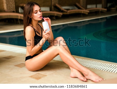 Beautiful young woman with cocktail in swimming pool and relaxing