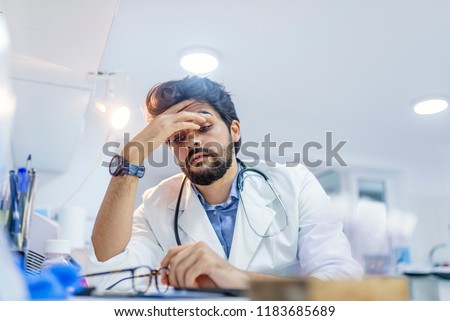Stressed male doctor sat at his desk. Mid adult male doctor working long hours. Overworked doctor in his office. Not even doctors are exempt from burnout . 