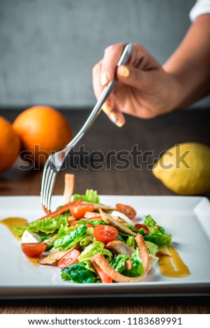 Salad with cherry tomatoes, salmon, chicken, pepper, green leaves and egg on plate. Women hand with forks in frame. Delicious recipe with lemon sauce. Сolorful picture, orange and lemon on background