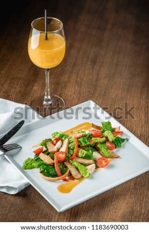 Salad with cherry tomatoes, salmon, chicken, pepper, green leaves and egg on plate. Delicious recipe with lemon sauce. Сolorful picture, wooden table, orange juice in wineglass. Place for text
