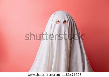 young child dressed in a ghost costume for halloween on pink background.